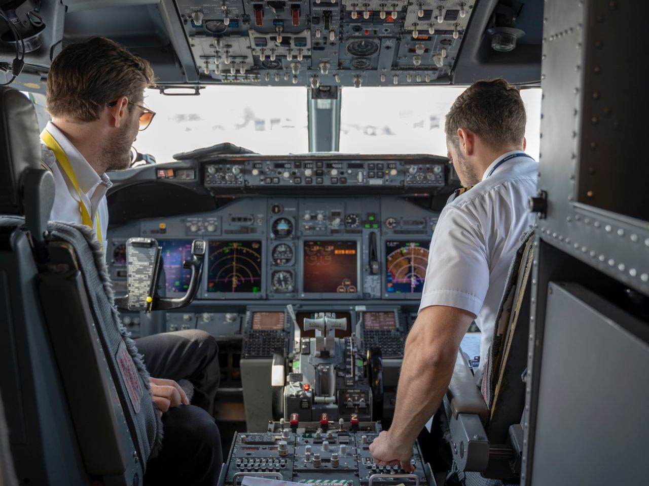 about-01 Two pilots navigating an aircraft cockpit, focused on advanced avionics and flight systems.