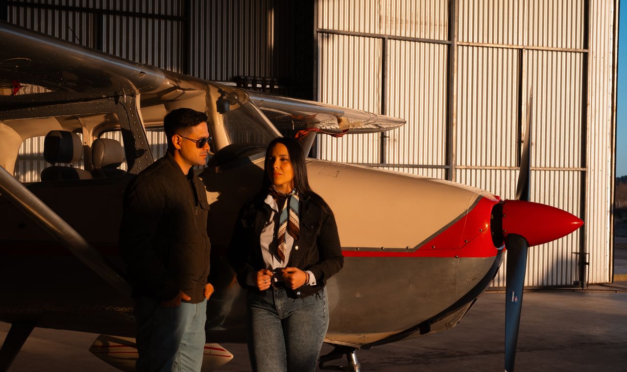 services-01 A fashionable couple standing by a small aircraft in a sunlit hangar.